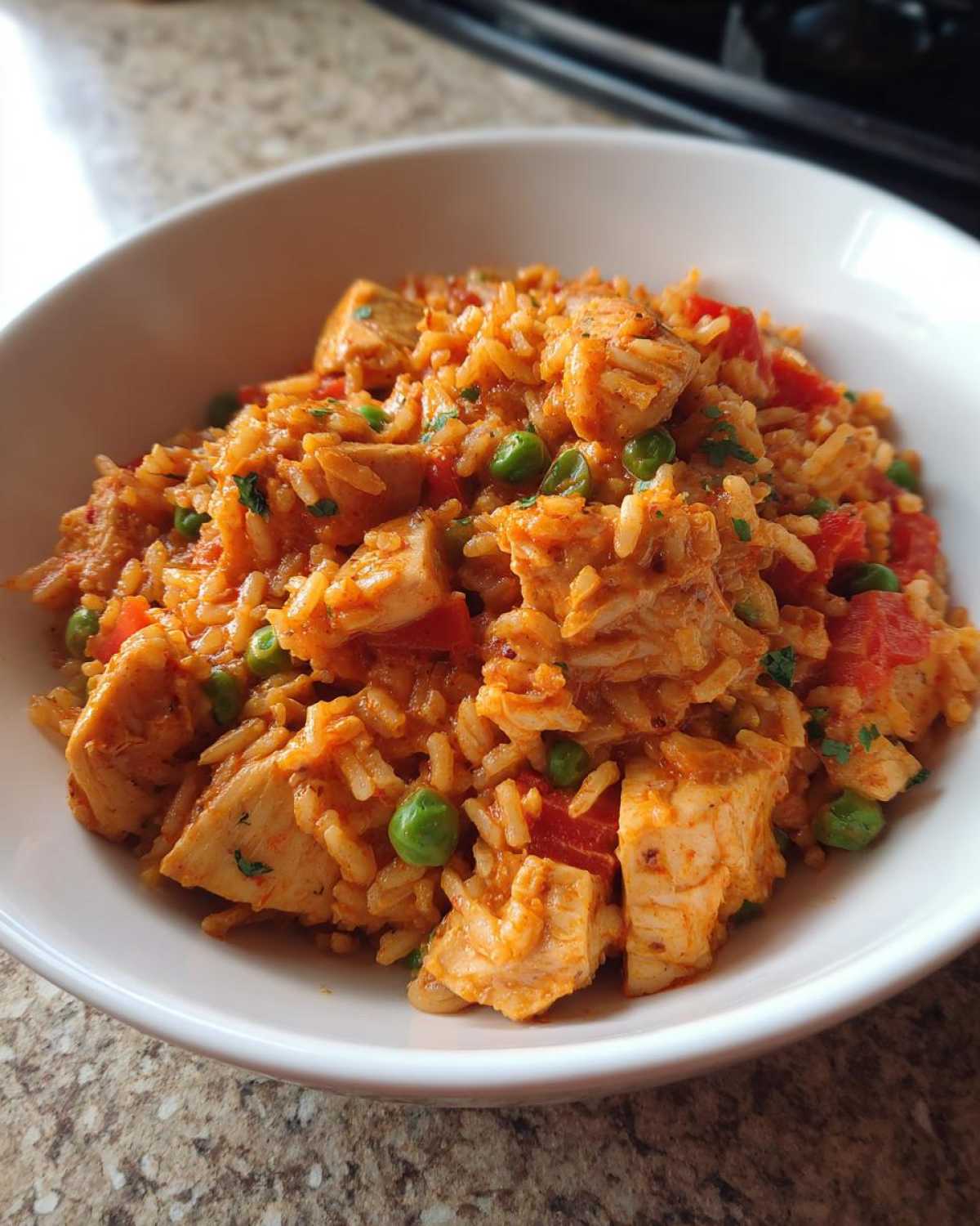 A close-up view of a white bowl filled with Creamy Cajun Chicken and Rice Skillet, featuring chunks of chicken, rice, peas, and tomatoes.