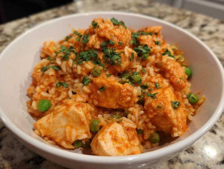A white bowl filled with Creamy Cajun Chicken and Rice Skillet, featuring chunks of chicken, rice, and green peas, topped with parsley.
