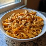 A close-up of a white bowl filled with rich, orange-hued Creamy Cajun Chicken Pasta with Garlic Flavor, topped with seasoned chicken pieces.