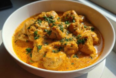 Close-up of tender chicken pieces smothered in a rich, orange-hued Creamy Cajun Chicken Skillet with Cream Sauce, garnished with parsley.