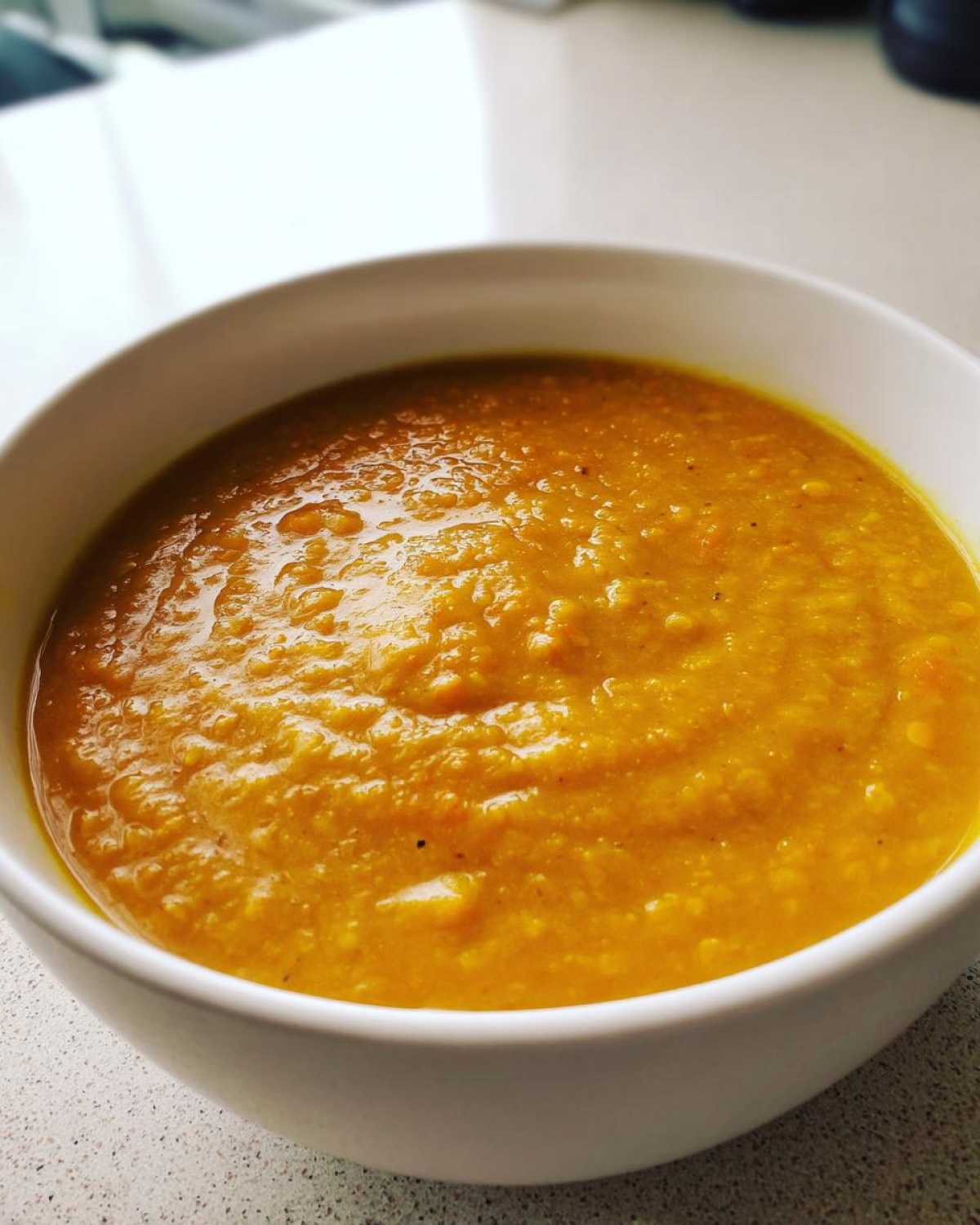 Close-up of a white bowl filled with thick, vibrant orange Creamy Coconut Lentil Soup.