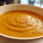 Close-up of a white bowl filled with vibrant orange Creamy Coconut Lentil Soup, showing a rich, thick texture.