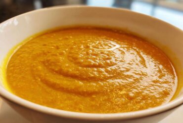 Close-up of a white bowl filled with vibrant orange Creamy Coconut Lentil Soup, showing a rich, thick texture.