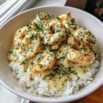 Close-up of a white bowl filled with white rice topped generously with Creamy Garlic Shrimp and fresh parsley.