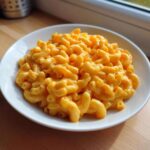 A close-up of a generous serving of creamy, bright orange Instant Pot Mac and Cheese in a white bowl.