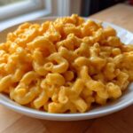 A close-up of a white bowl filled with rich, creamy Instant Pot Mac and Cheese, featuring elbow macaroni coated in bright orange cheese sauce.
