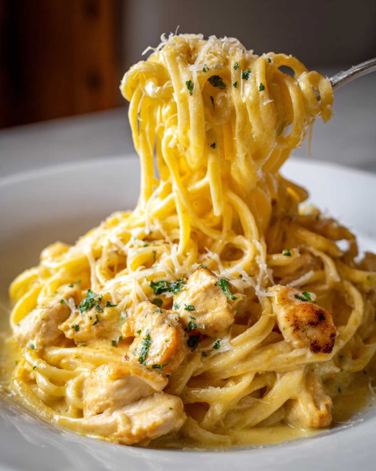 A fork twirls long strands of Creamy Lemon Chicken Pasta with Parmesan, topped with chicken pieces and parsley.