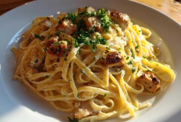 A close-up of Creamy Lemon Garlic Pasta with Chicken, featuring fettuccine coated in a rich sauce and topped with seared chicken pieces and parsley.