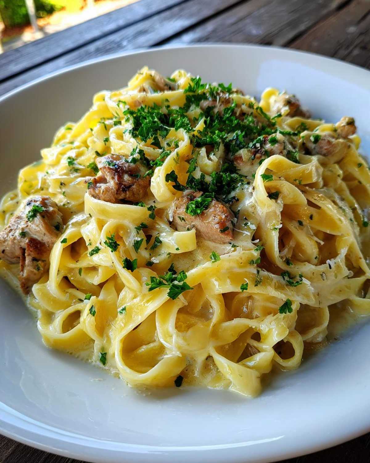 Close-up of fettuccine in a creamy sauce with chunks of chicken, topped with fresh parsley, representing Creamy Lemon Garlic Pasta with Chicken.