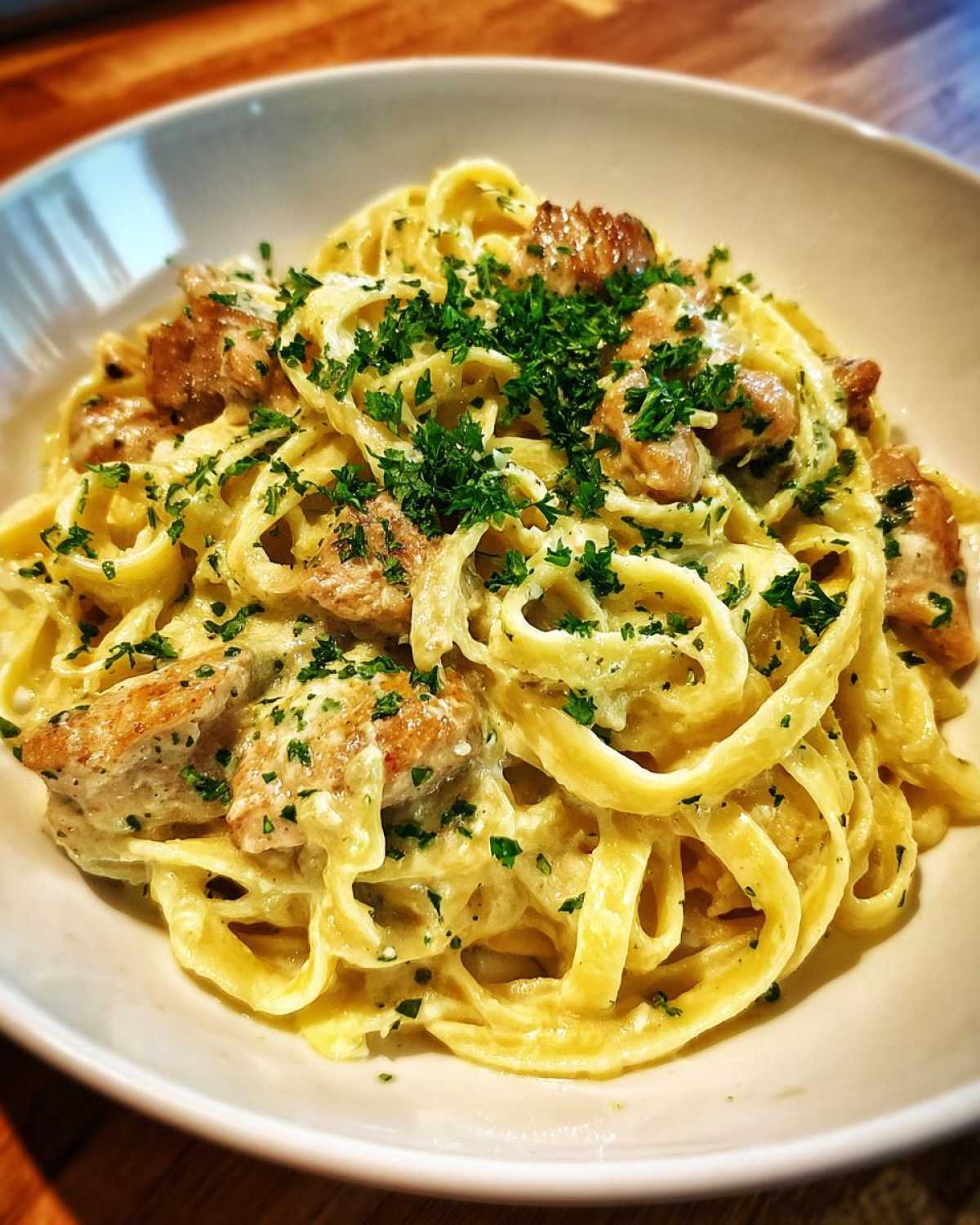 Close-up of fettuccine in a creamy sauce with chunks of chicken, topped with fresh parsley, part of the Creamy Lemon Garlic Pasta with Chicken.