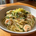A close-up view of a bowl filled with Creamy Lemon Garlic Shrimp Pasta, topped with fresh parsley and bright yellow lemon zest.