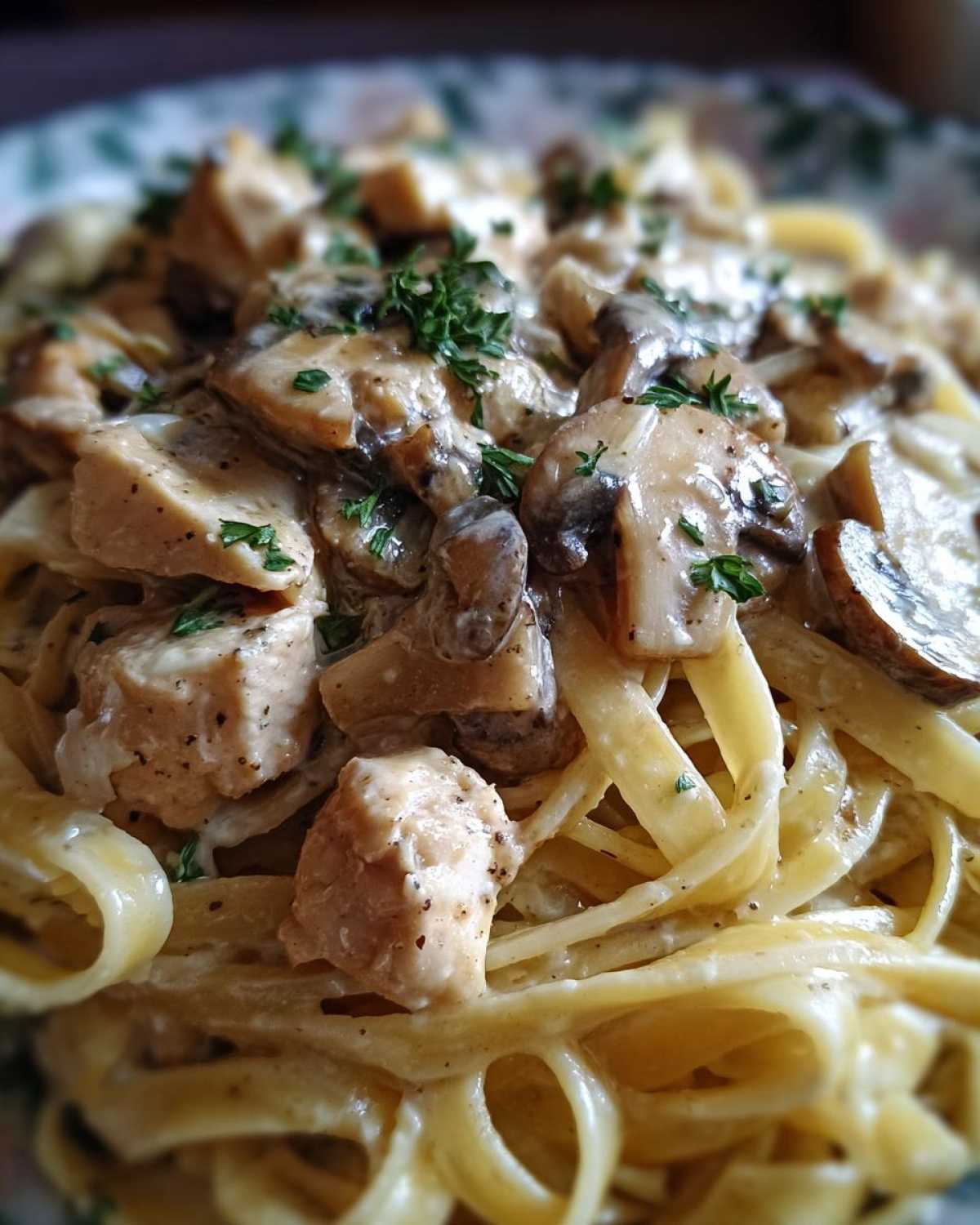 A close-up view of rich Creamy Mushroom Chicken Pasta with fettuccine noodles coated in a garlic sauce and topped with herbs.