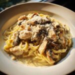 A close-up of Creamy Mushroom Chicken Pasta with Parmesan served in a white bowl, topped with grated cheese.