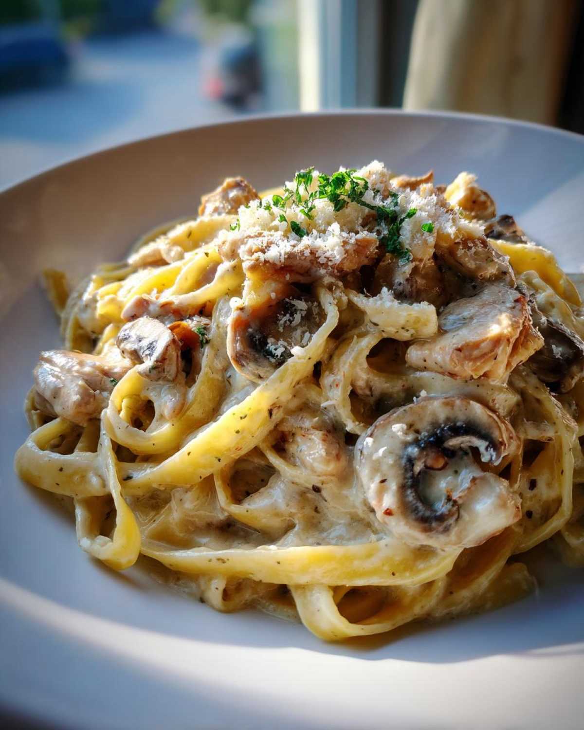 Close-up of a bowl of Creamy Mushroom Chicken Pasta with Parmesan, topped with grated cheese and parsley.