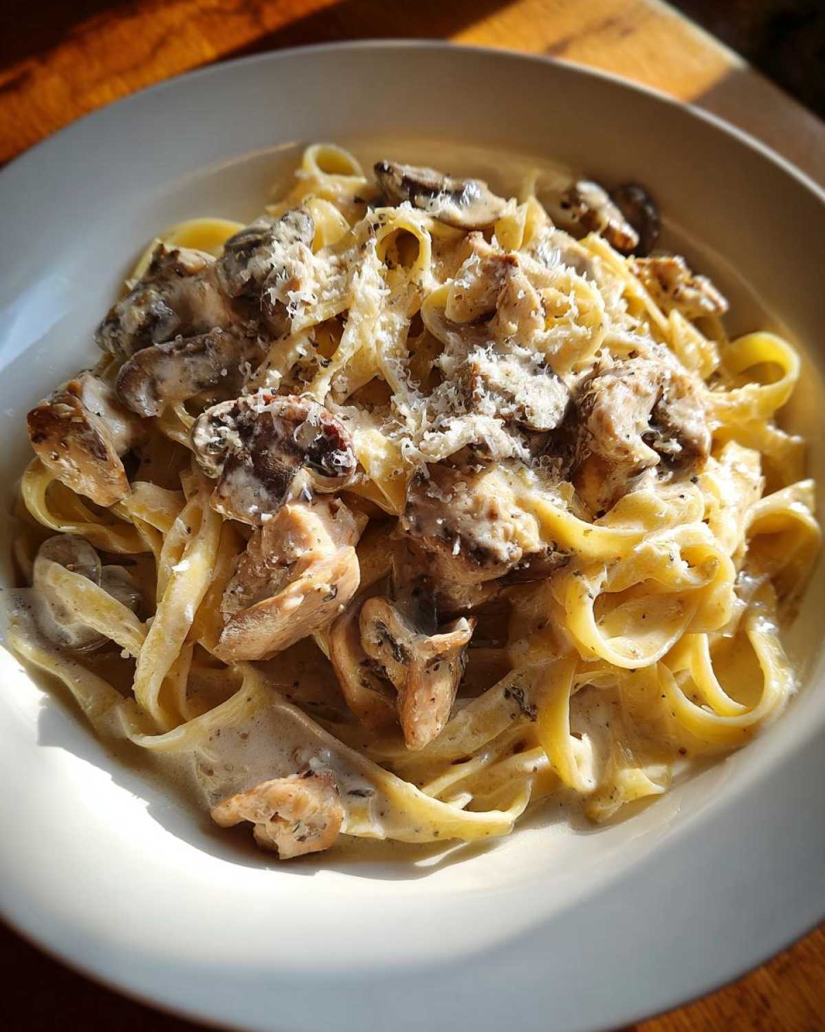 A close-up of rich Creamy Mushroom Chicken Pasta with Parmesan, featuring fettuccine coated in sauce.