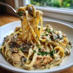 A fork lifts fettuccine noodles coated in sauce from a bowl of Creamy Mushroom Garlic Pasta with Chicken, garnished with parsley.