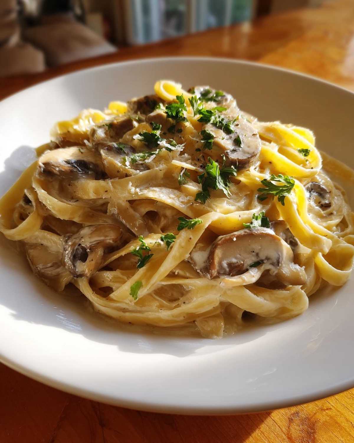 A close-up of fettuccine pasta coated in a rich Creamy Mushroom Pasta with Parmesan Sauce, topped with sliced mushrooms and fresh parsley.