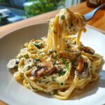 A fork lifting fettuccine noodles coated in Creamy Mushroom Pasta with Parmesan Sauce, garnished with parsley.