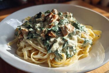 A close-up of fettuccine pasta topped generously with creamy sauce, spinach, and chunks of chicken in the Creamy Spinach Alfredo Pasta with Chicken.