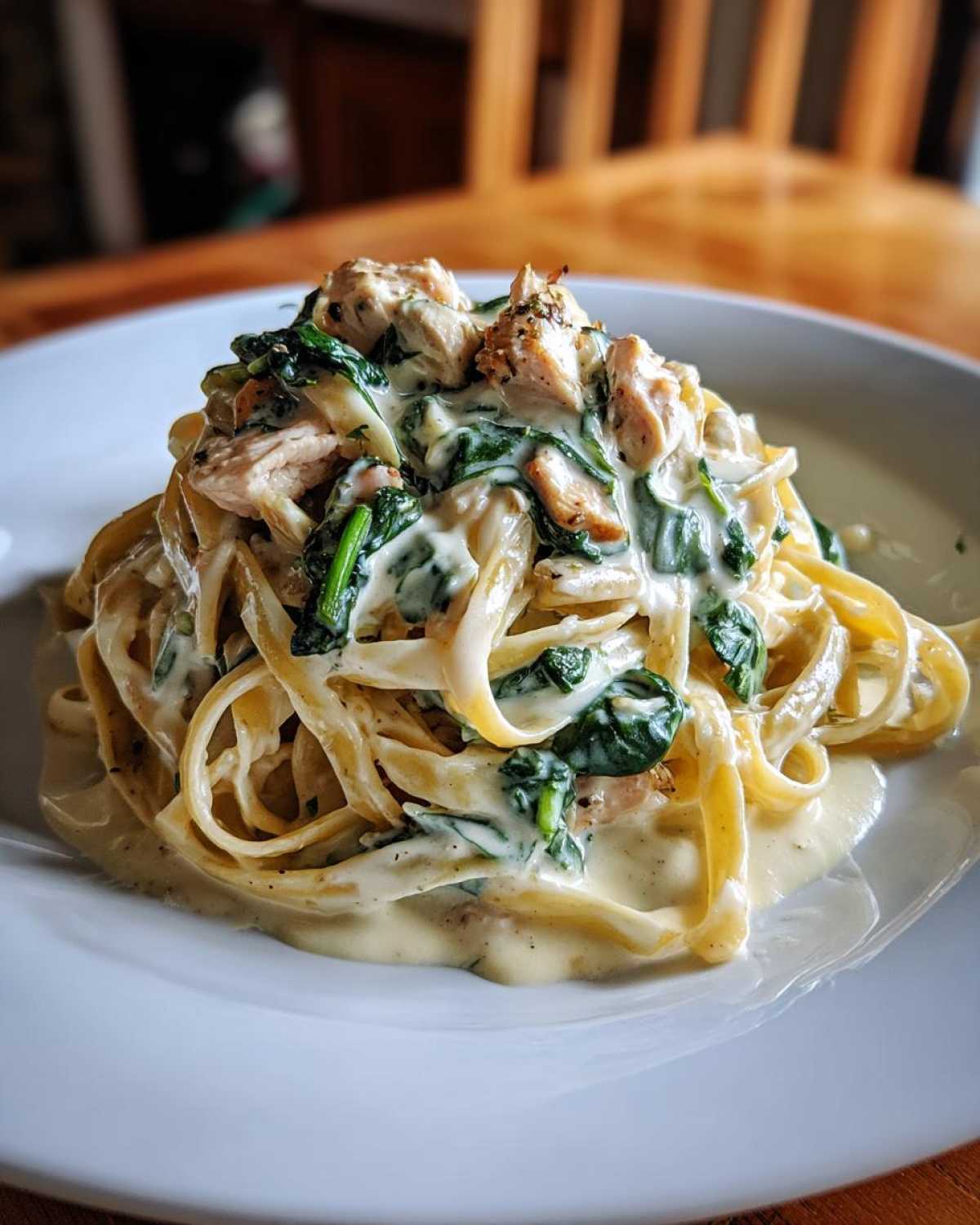 A generous serving of Creamy Spinach Alfredo Pasta with Chicken piled high on a white plate.