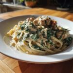 A close-up of a white bowl filled with Creamy Spinach Alfredo Pasta with Chicken, coated in rich white sauce.