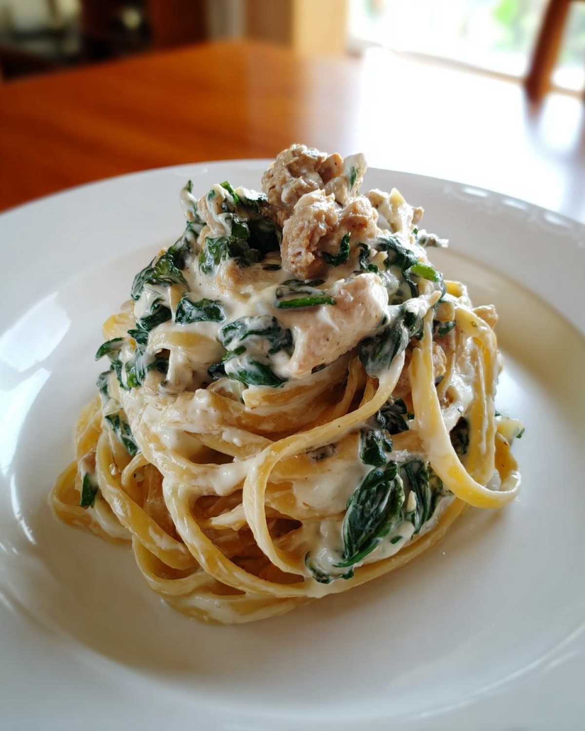 Close-up of a serving of Creamy Spinach Alfredo Pasta with Chicken tossed in rich white sauce on a white plate.