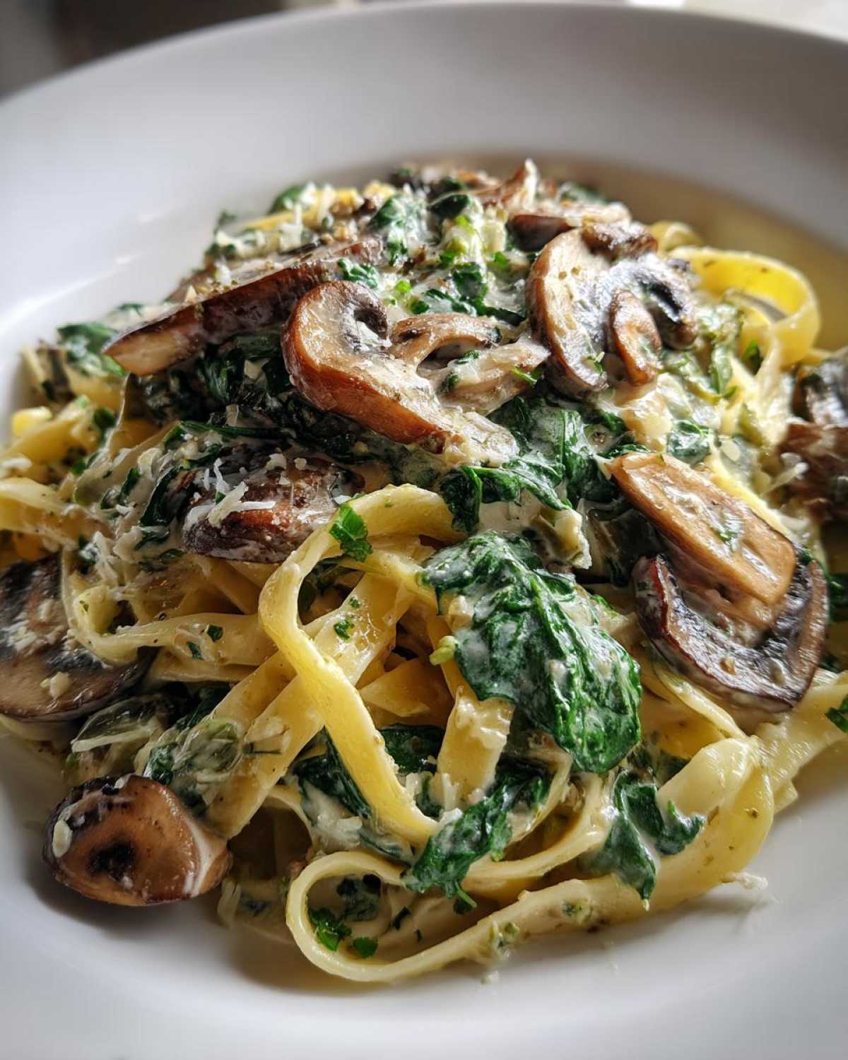 Close-up of fettuccine pasta coated in a creamy sauce with wilted spinach and sliced mushrooms, a perfect Creamy Spinach and Mushroom Pasta Dinner.
