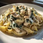 A close-up of creamy spinach chicken pasta with Alfredo sauce served on a white plate.