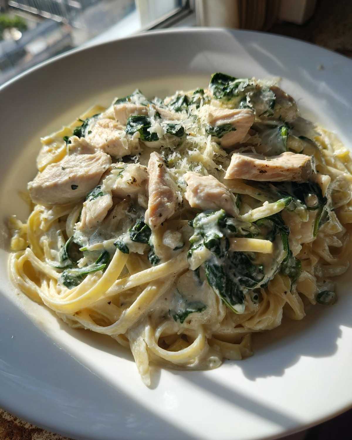 Close-up of a white bowl filled with Creamy Spinach Chicken Pasta with Alfredo Sauce, topped with grated cheese.