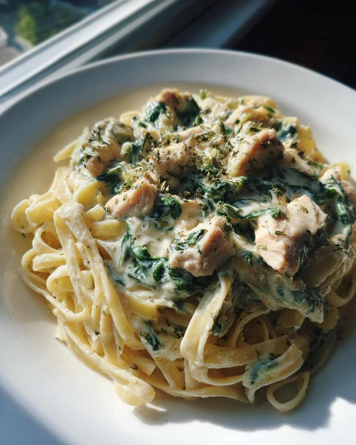 Close-up of Creamy Spinach Chicken Pasta with Alfredo Sauce, featuring fettuccine, chicken chunks, and herbs.