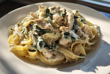 A close-up of creamy spinach chicken pasta with Alfredo sauce served on a white plate.
