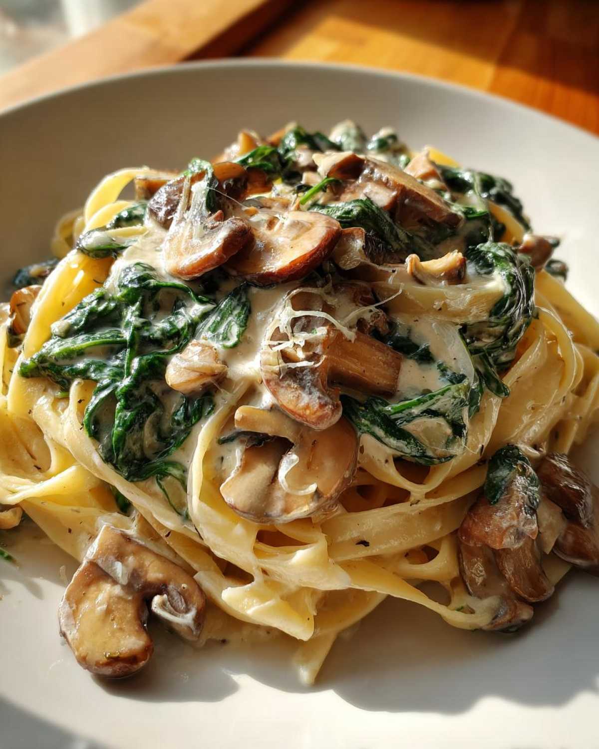 A close-up view of fettuccine pasta tossed in a rich cream sauce with sautéed mushrooms and wilted spinach, part of the Creamy Spinach and Mushroom Pasta Dinner.