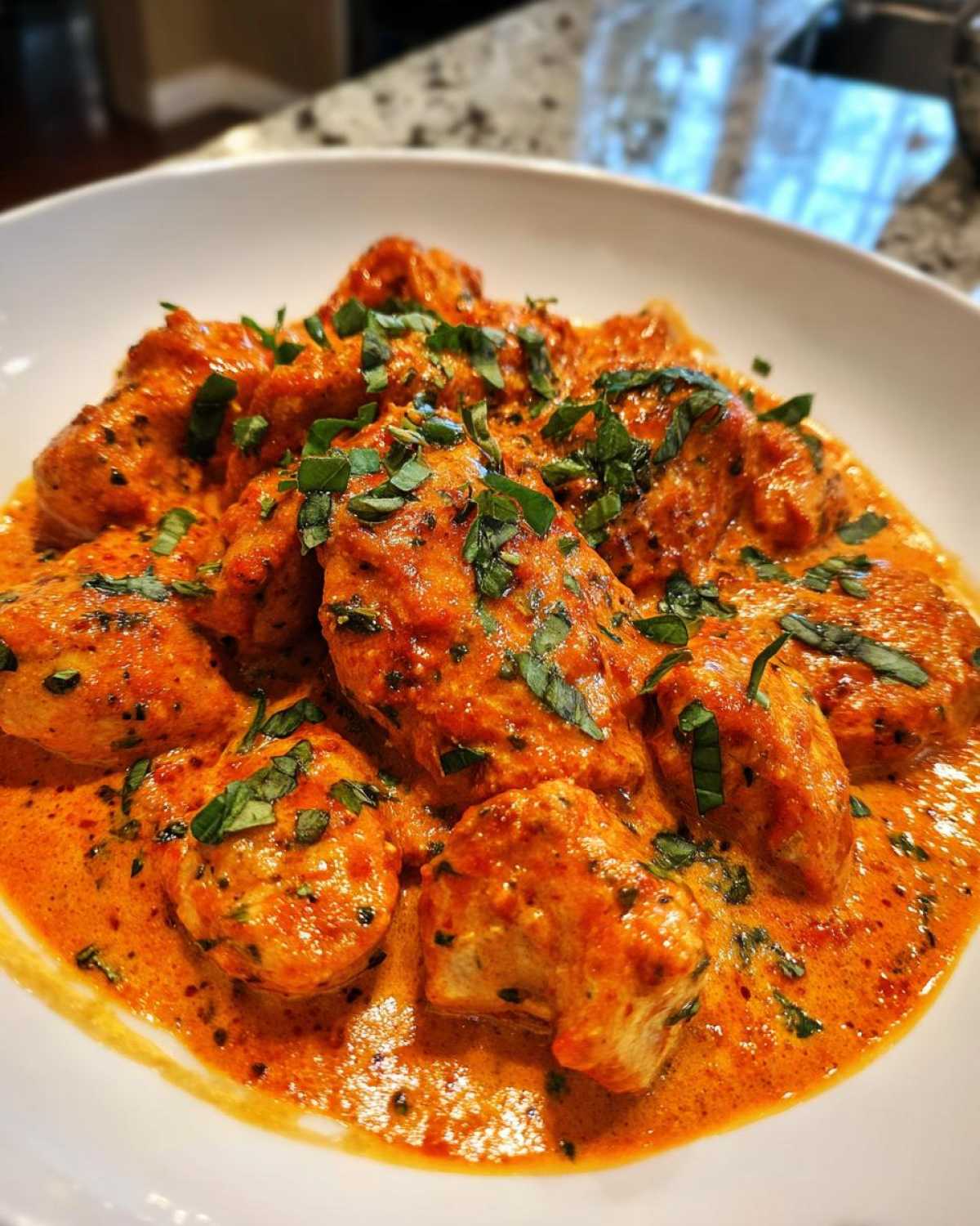 Close-up of bite-sized chicken pieces smothered in a rich, orange-red sauce in the Creamy Tomato Basil Chicken Skillet recipe.