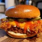 A close-up of a Crispy Chicken Sandwich with Honey Sauce, topped with melted cheese and pickles on a brioche bun.