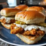 Two delicious Crispy Chicken Sliders with garlic sauce and pickles served on a blue plate.