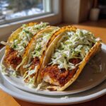 Three assembled Crispy Chicken Tacos featuring golden fried chicken and creamy slaw piled high on warm tortillas.