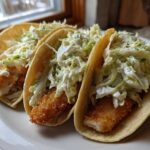Three Crispy Chicken Tacos generously topped with creamy slaw, served on a white plate.