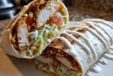 Cross-section of a Crispy Chicken Wrap with Ranch Sauce, showing fried chicken, lettuce, tomato, and a drizzle of white sauce.
