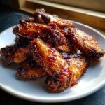 A pile of crispy Honey Garlic Chicken Wings oven baked, coated in a thick, glossy glaze, served on a white plate.