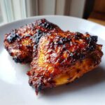 Two pieces of Honey Soy Chicken Thighs with Crispy Edges, glazed and caramelized, resting on a white plate.