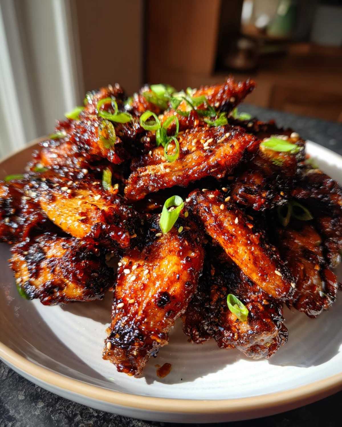 A pile of glossy, dark, crispy Honey Soy Chicken Wings Crispy Oven Baked garnished with sesame seeds and green onions.