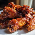 A pile of crispy oven Sticky Sweet Chili Chicken Wings glistening with a thick, dark glaze and sesame seeds.