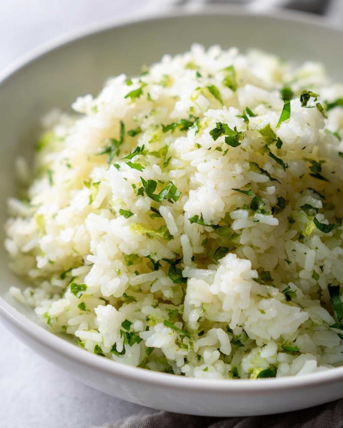 Close-up of fluffy Cilantro Lime Rice mixed with bright green chopped cilantro and lime zest in a white bowl.