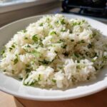 A close-up of fluffy Cilantro Lime Rice mixed with bright green chopped cilantro, served in a white bowl.