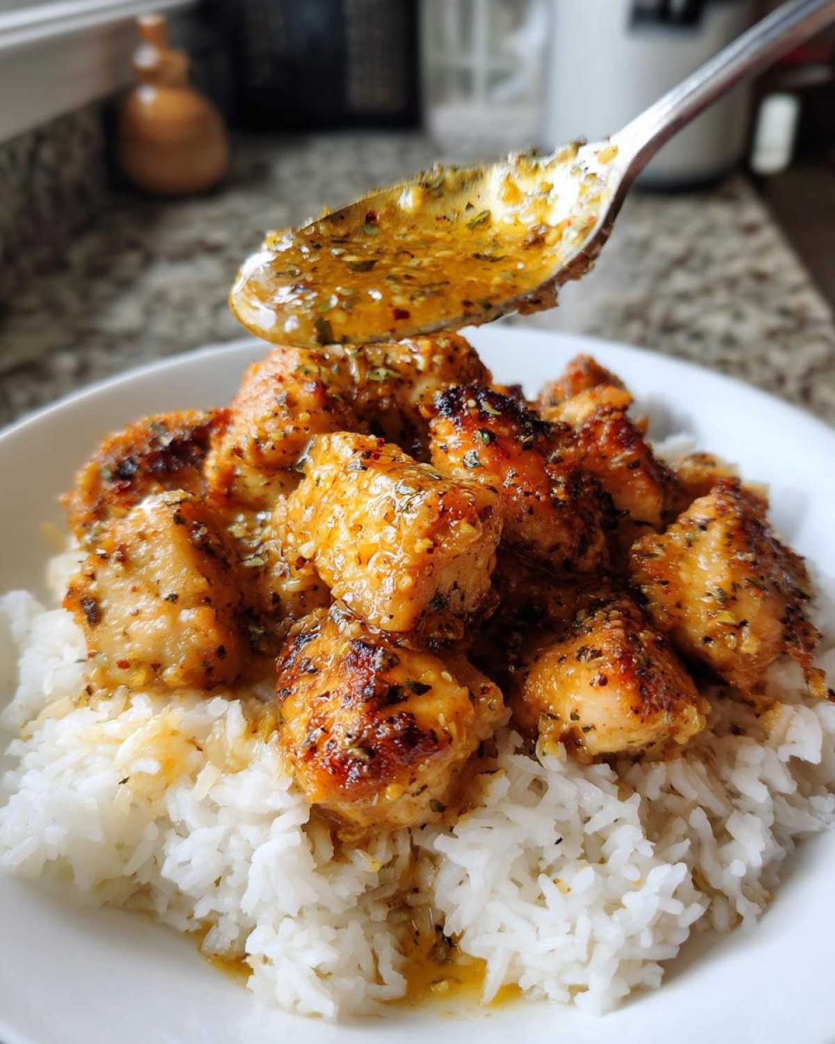 A spoon drizzles rich garlic butter sauce over golden Garlic Butter Chicken Bites served on a bed of white rice.