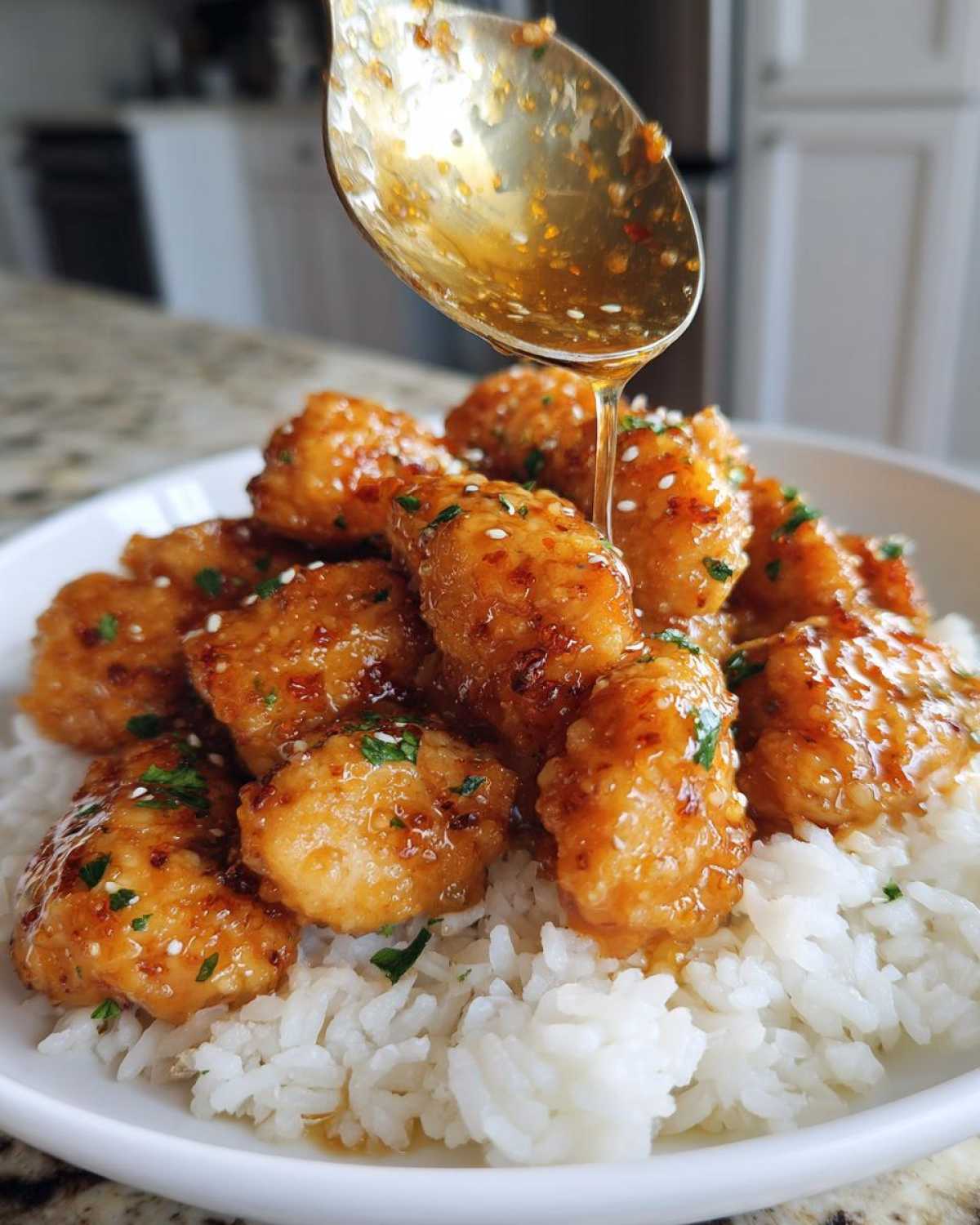 Close-up of Garlic Butter Chicken Bites being drizzled with sauce from a spoon over white rice.