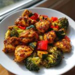 Close-up of Garlic Butter Chicken Bites served with roasted broccoli, zucchini, and red peppers on a white plate.