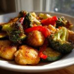 Close-up of golden Garlic Butter Chicken Bites mixed with roasted broccoli, zucchini, and red peppers on a white plate.