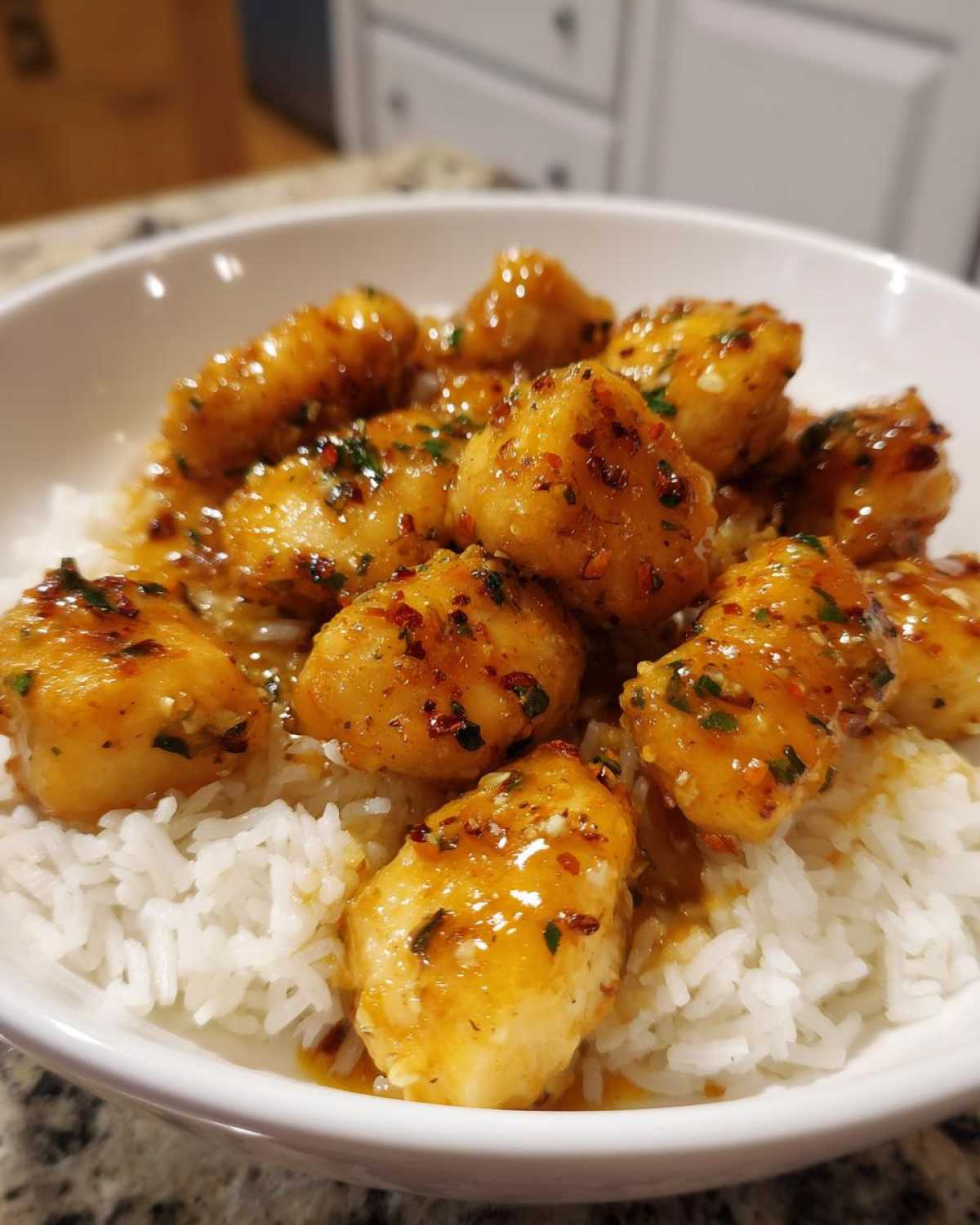 Close-up of Garlic Butter Chicken Bites coated in a glossy sauce, served over a bed of fluffy white rice in a white bowl.