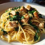A close-up of a white plate filled with Garlic Butter Pasta with Chicken and Spinach, glistening under natural light.